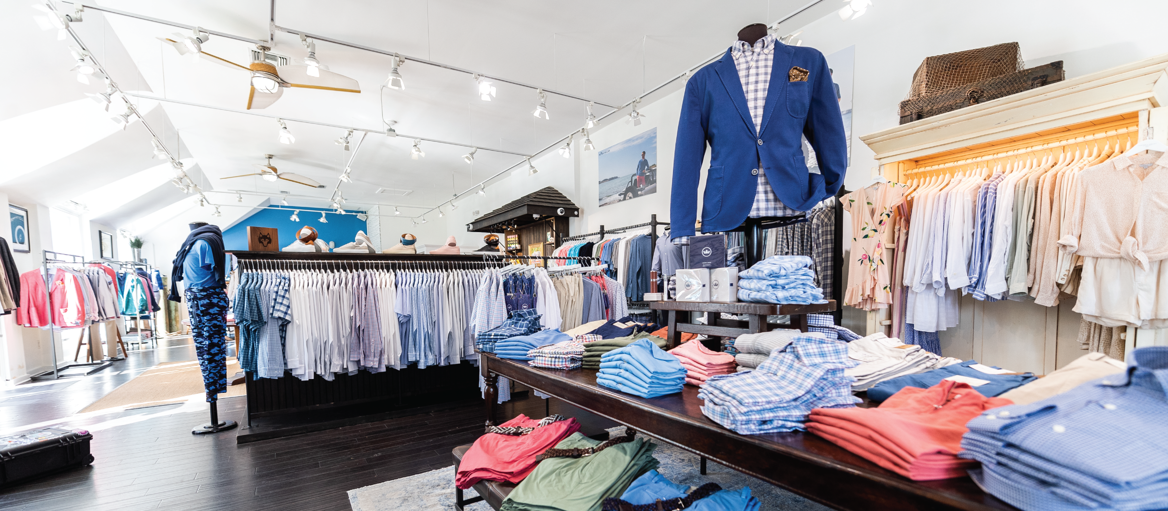 A brightly lit clothing store with neatly arranged racks of men's shirts and suits. Colorful folded clothes fill tables, creating a clean, inviting atmosphere.